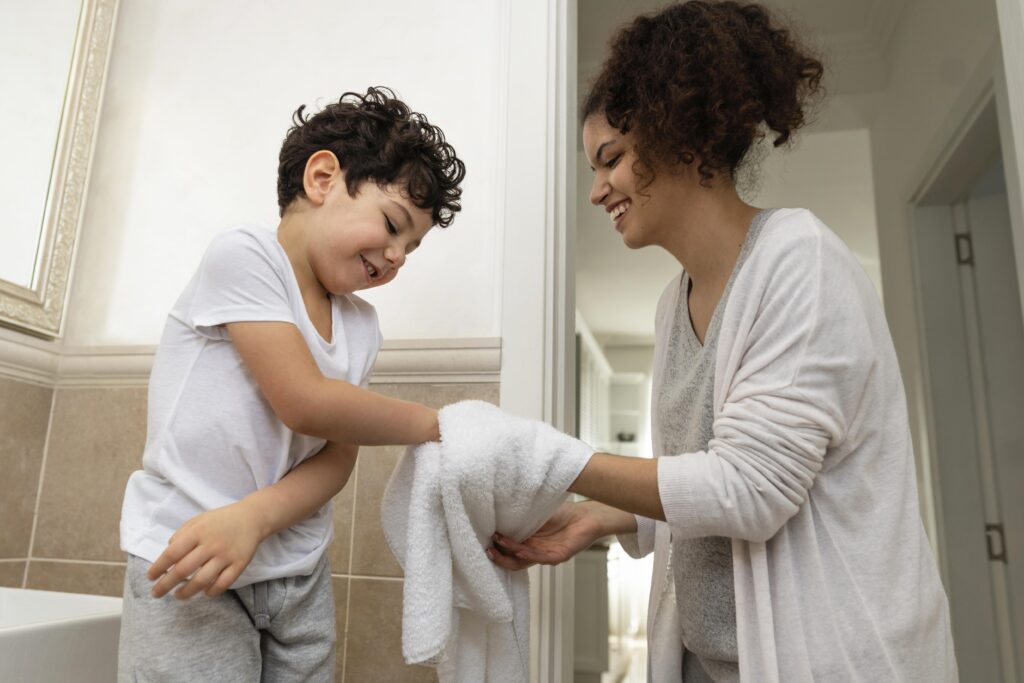 Mother lovingly drying child's hands with a towel after washing them in the bathroom, promoting good hygiene and care.